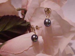 [ 6.5mm by 8.5mm oval black pearl earrings dangling from a 14K gold heart. ]